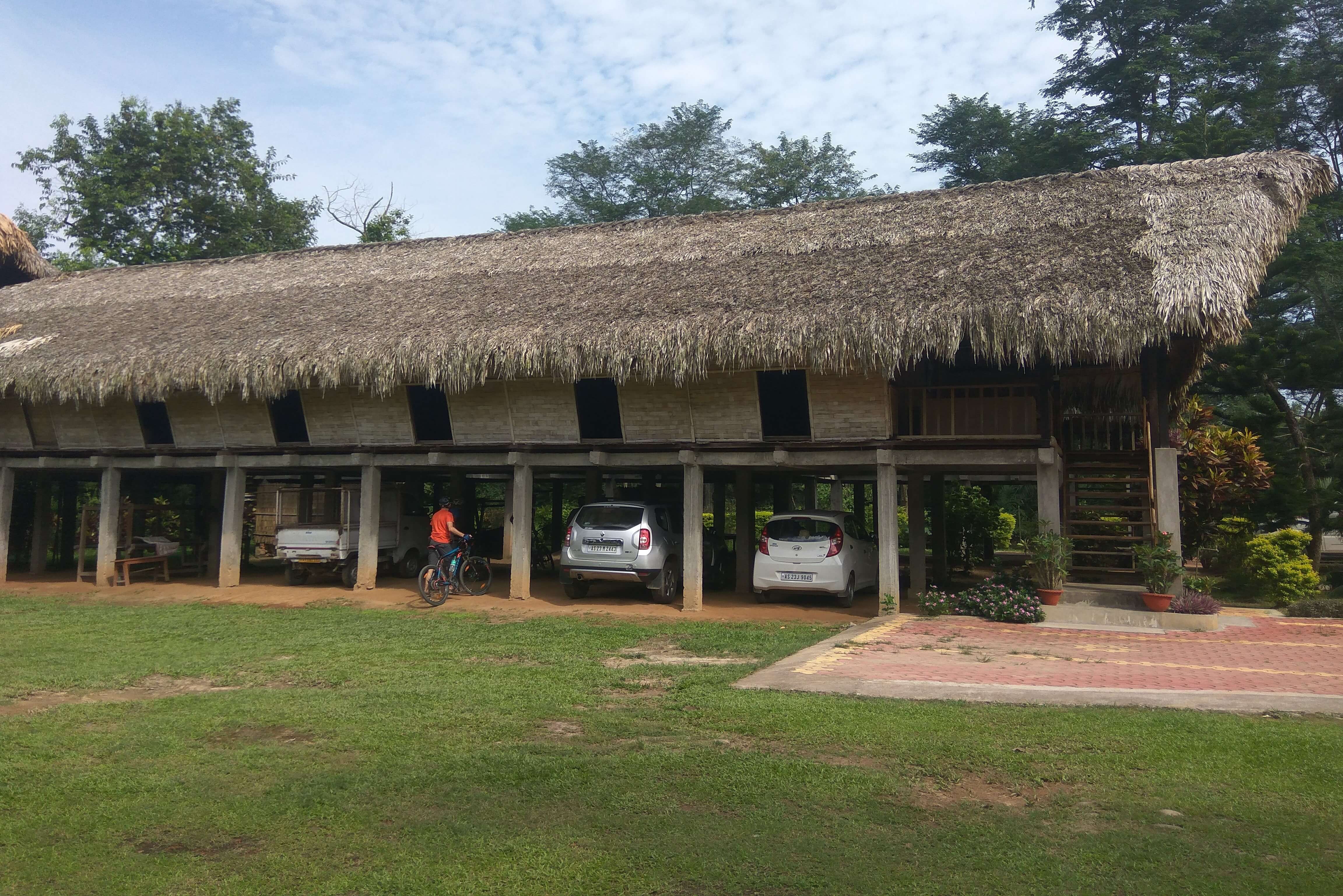 A long straw hut on stilts with a cyclist parking their gear underneath